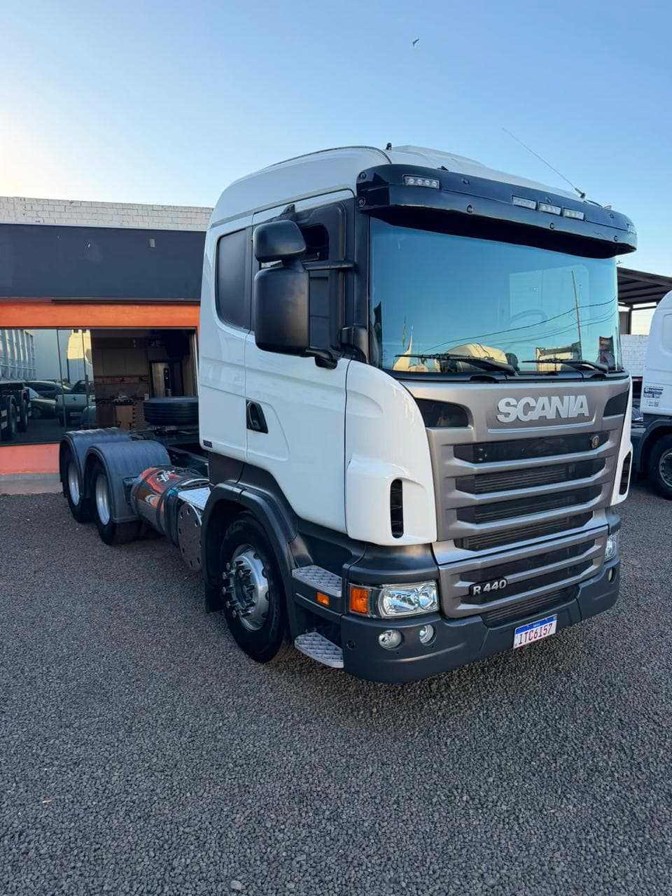 Frente de caminhão branco Scania estacionado em pátio de brita.